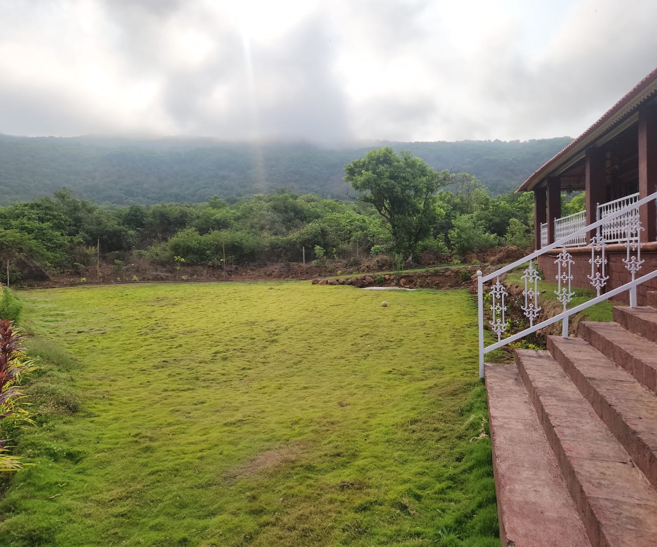 Lush green grounds of Red Stone Villa with misty Sahyadri mountains