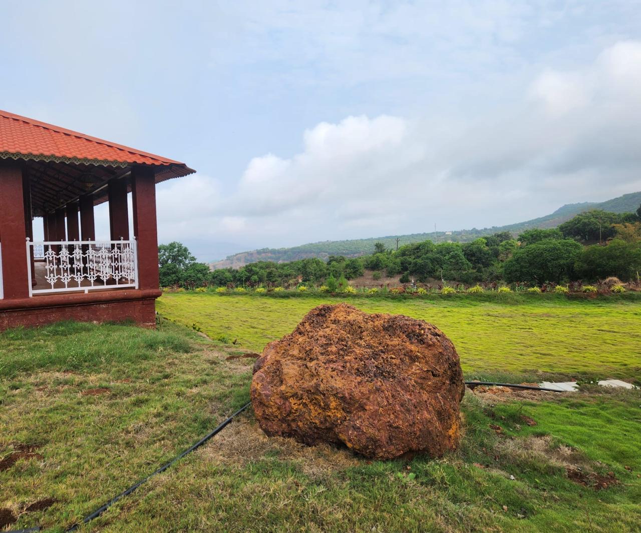 Red Stone Villa with ancient laterite boulder in the foreground against Sahyadri mountain backdrop